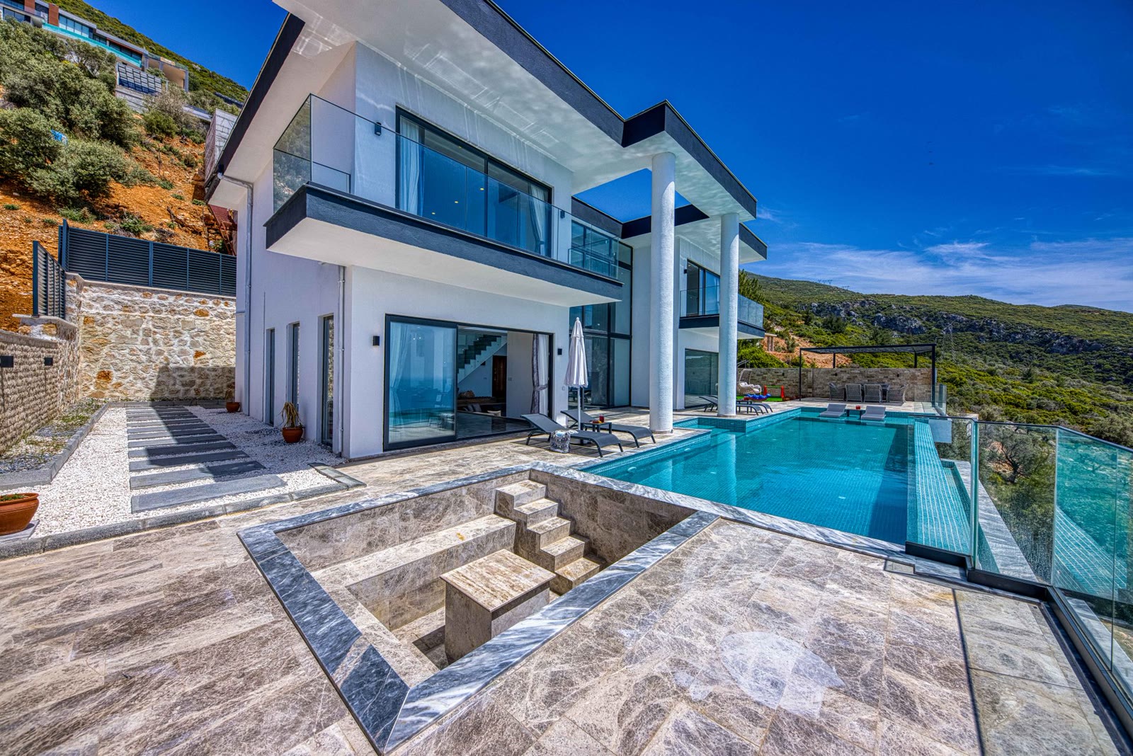 Infinity pool with stone-clad terrace overlooking hillside
